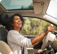 A woman smiles broadly as she drives during summertime. 